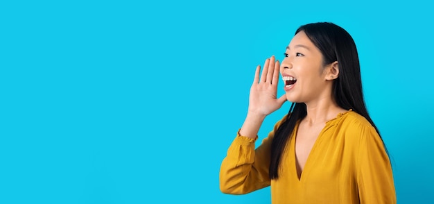 Cheerful chinese lady holding hand next to mouth screaming something