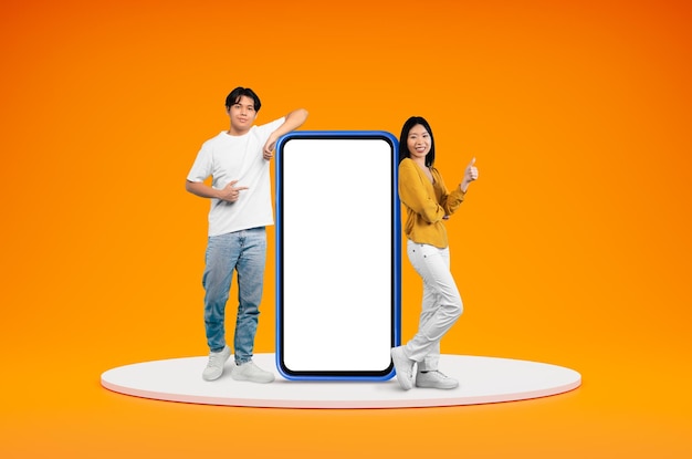 Cheerful chinese millennials posing by big phone showing thumb up