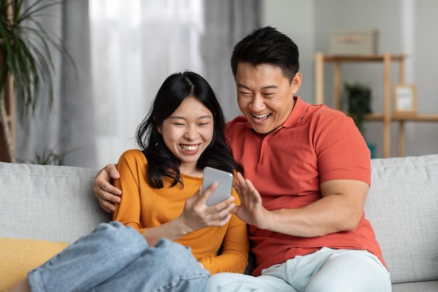 Cheerful chinese spouses using cell phone home interior