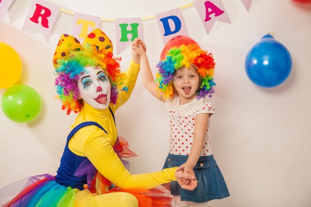 Cheerful clown girl on the holiday shows emotions with the birthday girl