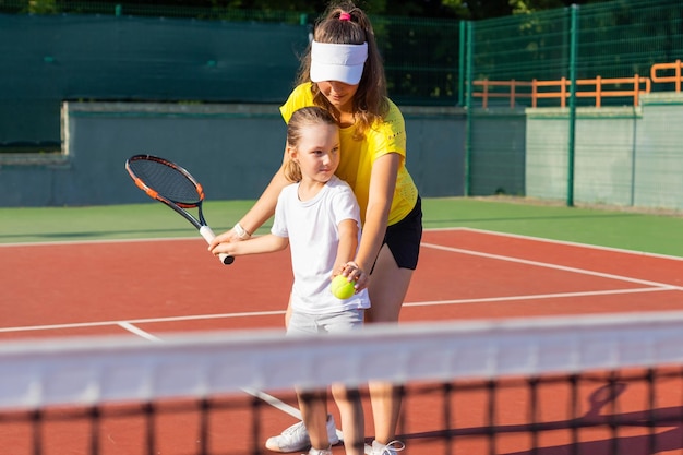 Веселый тренер в спортивной одежде учит ребенка играть в теннис, пока оба стоят на теннисном корте