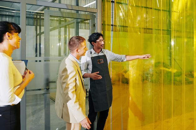 Cheerful coffee roastery owner showing factory rooms to business partners