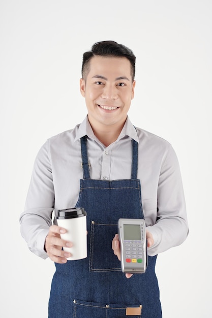 Cheerful coffeeshop barista giving cup of takeout coffee and payment terminal