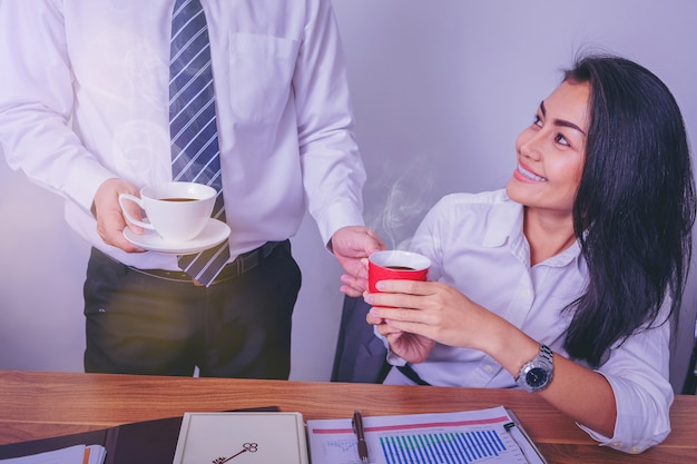 Cheerful colleagues sharing and enjoying coffee together in office.