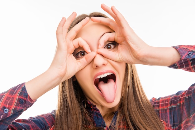 Cheerful comic girl holding fingers near eyes like glasses and showing tongue