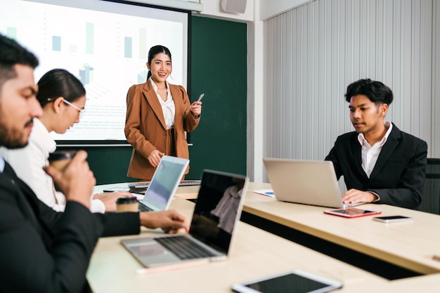 A cheerful and confident Asian businesswoman stands present bar charts data from projector screen