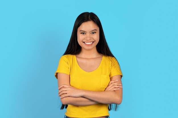 Cheerful confident pretty young chinese female in yellow tshirt with crossed arms on chest look at camera