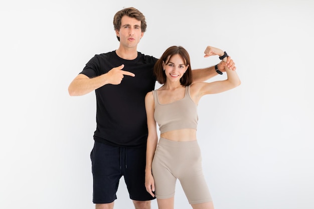 Cheerful confident young european couple in sportswear guy point finger on woman biceps