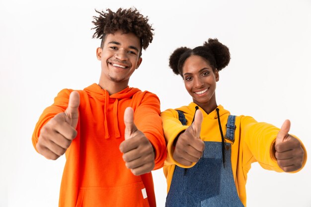 cheerful couple in colorful clothes showing thumbs up, isolated over white wall