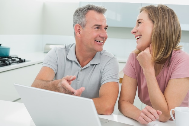 Coppie allegre nella conversazione mentre usando computer portatile nella cucina