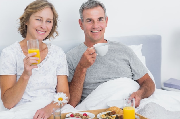 Cheerful couple having breakfast in bed together