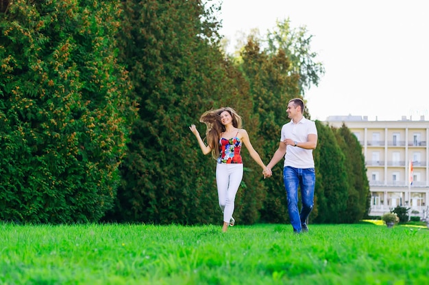 Cheerful couple holding hands runs on green grass in nature The woman waves her hair