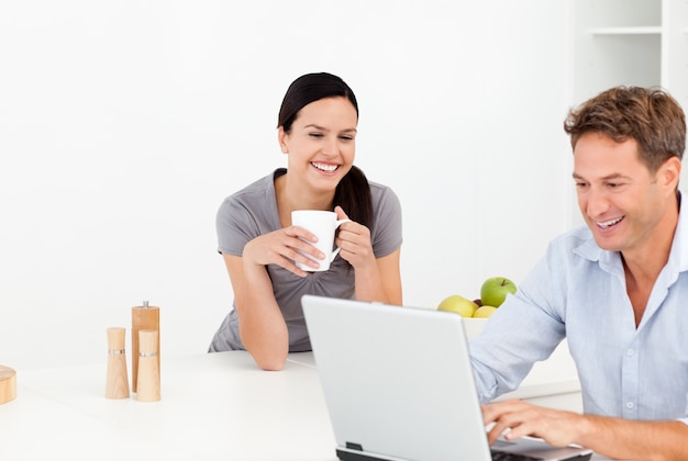 Cheerful couple looking at something on internet while drinking coffee