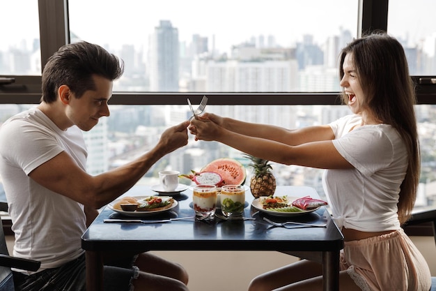 Cheerful couple playfully fights with cutlery during the breakfast