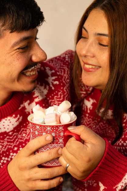 Photo cheerful couple sharing a cup of chocolate with many marshmallows at christmas