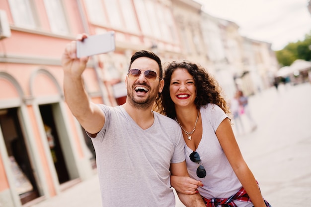 Cheerful couple taking selfie in a city on a vacation.