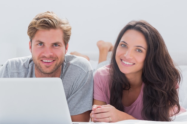 Cheerful couple using laptop in bed