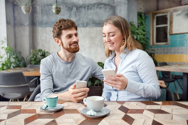 Cheerful couple with coffee and phone in cafe