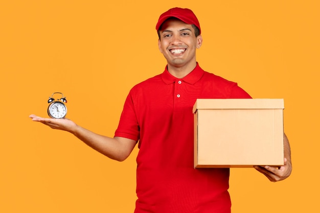 Cheerful courier guy holding parcel carton box and clock studio