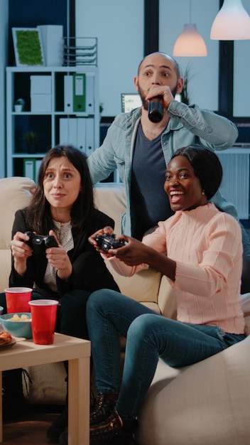 Cheerful coworkers playing video games with joysticks and\
console on television. workmates winning game with controllers on\
tv for entertainment, enjoying drinks and snacks after work