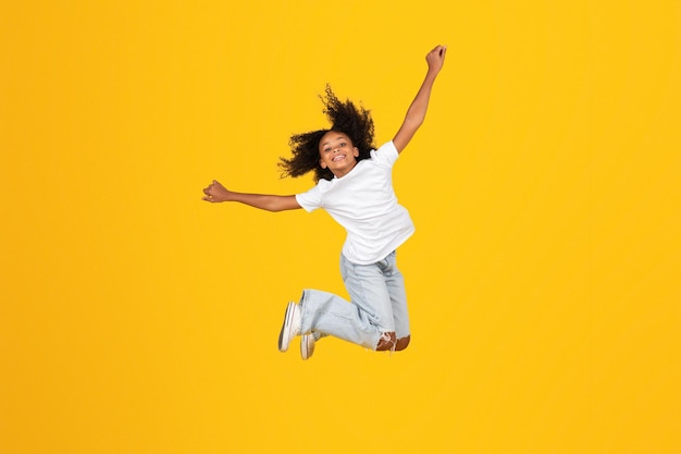 Cheerful curly teen black schoolgirl in white tshirt has fun jumping freezes in air enjoy freedom