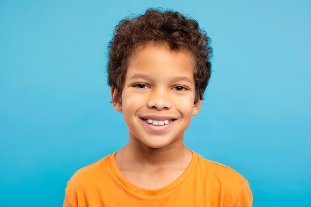 Cheerful curlyhaired boy in orange tshirt blue background