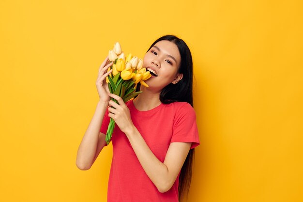 Cheerful cute asian girl with a bouquet of flowers yellow background