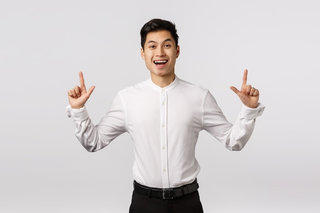 Cheerful cute asian guy celebrating birthday inviting guests see fireworks. Man rejoicing as standing in suit, pointing up, smiling happy and entertained, found product he liked,