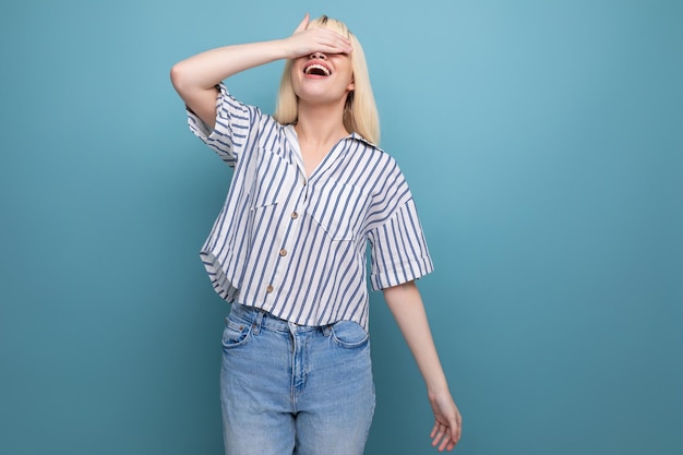 Cheerful cute blond year old female person in a striped blouse and jeans on a blue background