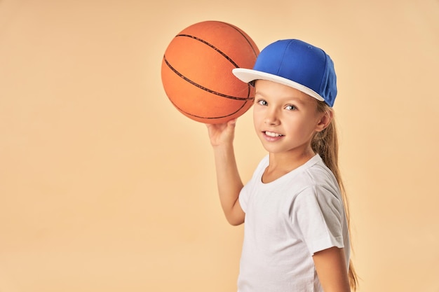 Cheerful cute girl in cap plying basketball