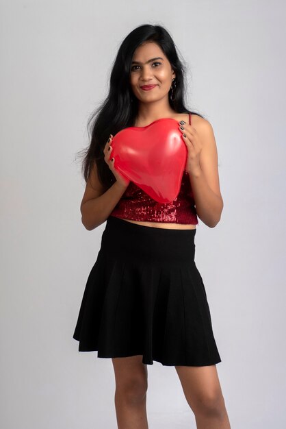 Cheerful cute girl in fancy outfit posing with heart shape balloon