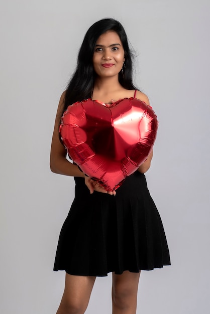 Cheerful cute girl in fancy outfit posing with heart shape balloon