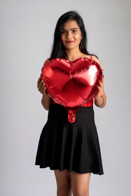 Cheerful cute girl in fancy red and black outfit posing with heart shape balloon.