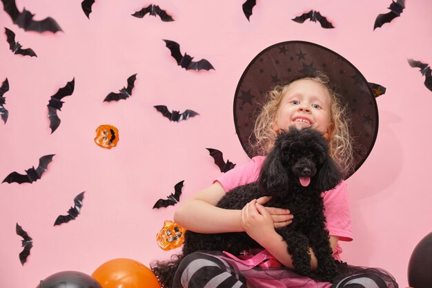 Cheerful cute girl and little black mini poodle on the background of halloween scenery