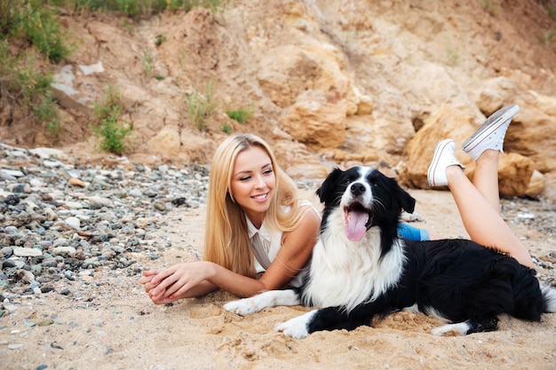 Ragazza carina allegra sdraiata e rilassante con il suo cane sulla spiaggia