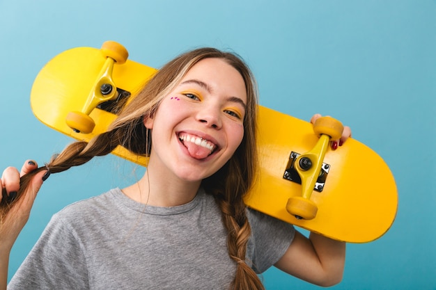 Cheerful cute girl standing isolated, holding skateboard