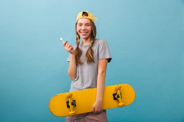 Cheerful cute girl standing isolated, holding skateboard