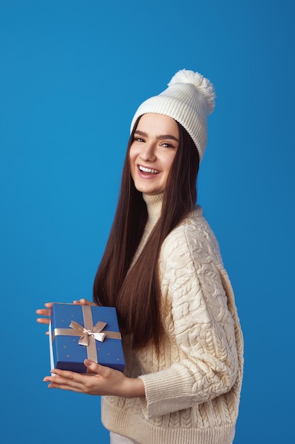 Cheerful cute girl wearing white oversize sweater and hat holding present