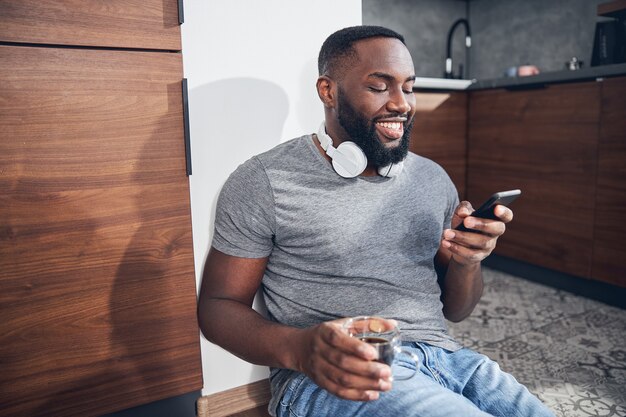 Cheerful darkskinned man sitting in the kitchen alone