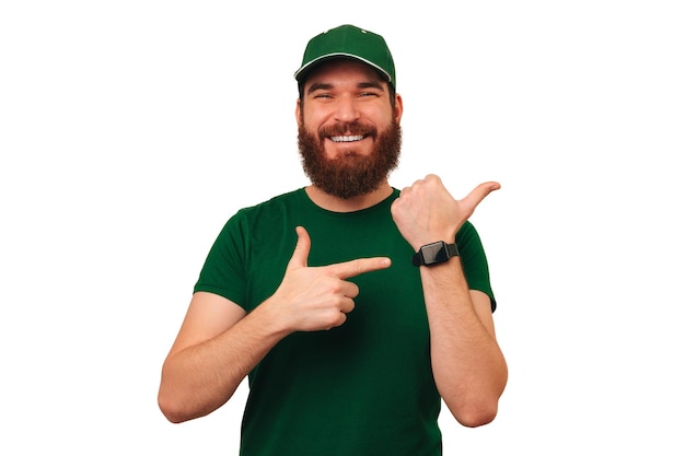 Cheerful delivery man wearing green uniform and smart watch points at it
