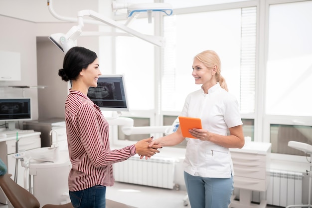 Cheerful dentist shaking hands with her new patient wishing her good morning