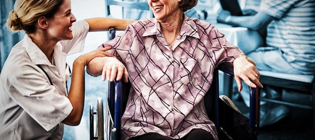 Cheerful disabled senior woman sitting on wheelchair looking at female doctor