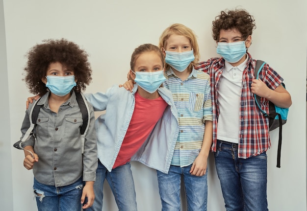 Cheerful diverse children wearing protective face masks looking at camera posing together over