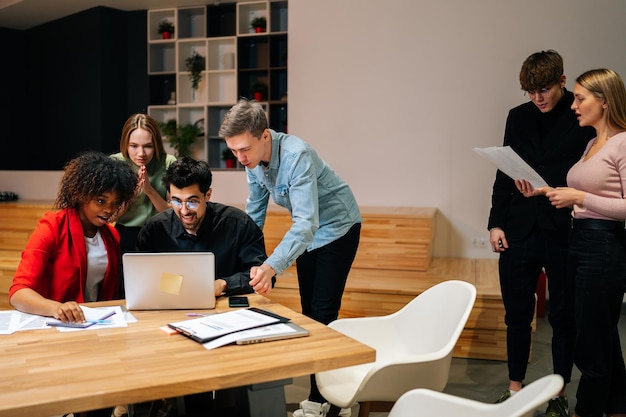 Cheerful diverse multiethnic creative millennial team excited by online result or growth good news business success looking at laptop laughing together