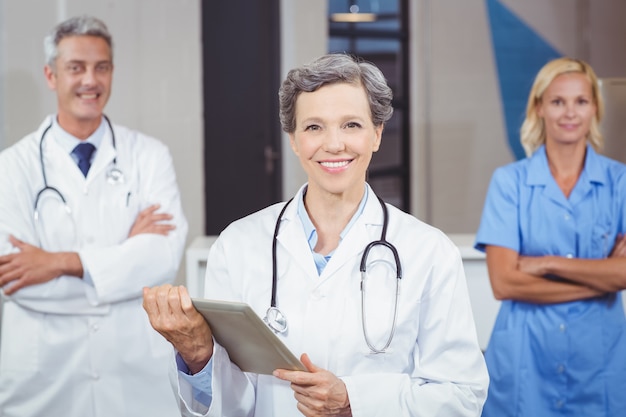 Cheerful doctor holding digital tablet while colleagues with arms crossed 