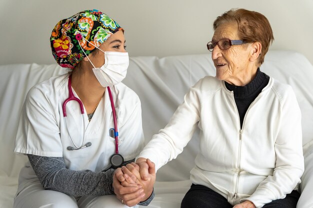 Foto medico allegro in maschera che tiene la mano della donna anziana