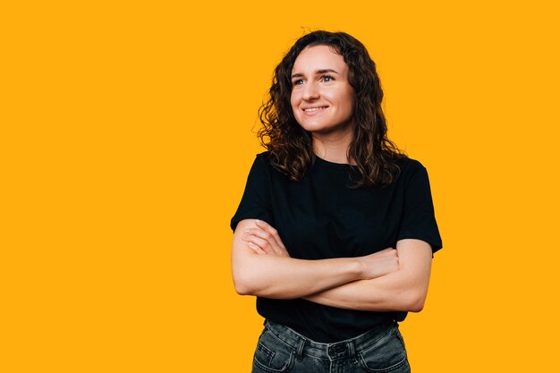 Cheerful dreamy young woman is holding arms crossed in a yellow studio