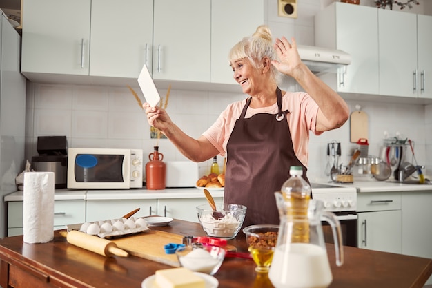 Веселая пожилая дама делает видеозвонок из кухни