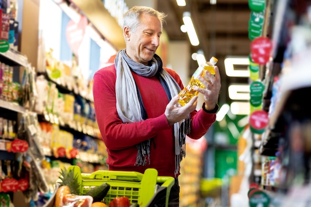Веселый пожилой мужчина выбирает масло в супермаркете