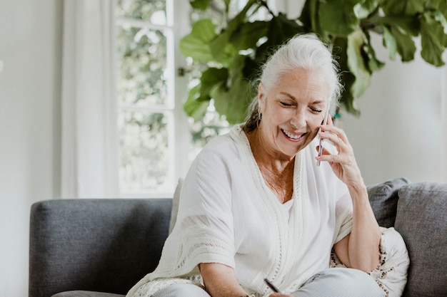 Cheerful elderly woman talking on a phone on a couch